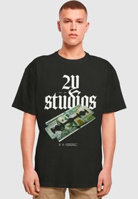 Melns kokvilnas T-krekls ar izteiksmīgu baltu tekstu "2U & studios" un grafiku, kurā attēlots dolāra rēķins ar skuvekļa asmeni dizainā priekšpusē.