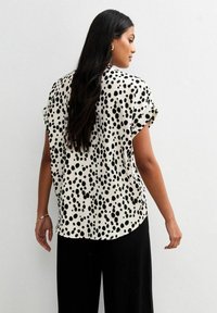 Blusa a maniche corte in tessuto leggero, con una base color crema e un motivo a macchie nere. Vestibilità rilassata con orlo arrotondato e maniche con risvolto.