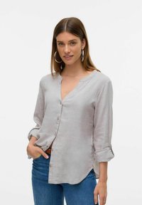 Chemise boutonnée gris clair avec un col arrondi, des manches retroussées et une coupe ample. Le tissu semble texturé et respirant.