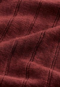 Gros plan sur un tissu rouge foncé texturé avec un motif côtelé vertical en tricot et des plis doux.