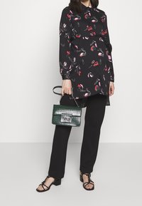 Svart skjortklänning med blommönster i rosa och rött, svarta byxor och en texturerad grön handväska med silverdetaljer. Svarta remsandaler.