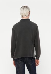 Long-sleeve dark gray polo shirt with a collar, relaxed fit, and visible stitching. Paired with dark denim jeans featuring back pockets.