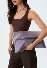 Clutch bag in camoscio viola con chiusura a zip, portato sotto il braccio. Texture liscia, forma rettangolare e design minimalista.