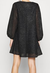 Vestido negro con un diseño de malla texturizada, que presenta mangas abullonadas y una silueta acampanada. Los acentos brillantes realzan su apariencia.