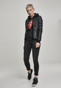 Black leather biker jacket, black hoodie with red logo, black skinny jeans, and black sneakers. Smooth leather texture and fitted design.
