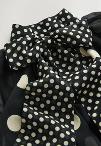 Nœud en tissu noir à pois blancs, noué proprement sur un vêtement noir à pois blancs assorti.