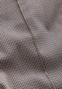 Tissu marron et bleu avec un motif à petits carreaux et une texture lisse ; couture visible le long de la couture.