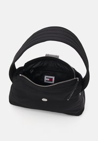 Sac à main en nylon noir avec une large anse matelassée et une fermeture zippée. L'intérieur comprend une poche zippée et une étiquette de marque. Accents en matériel argenté.