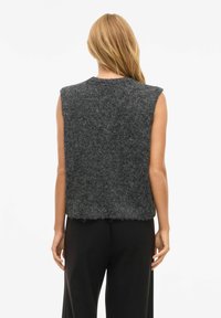 Bezroku pelēks vilnas džemperis ar fakturētu apdari, apaļu kakla izgriezumu un neapstrādātu apakšmalu, kombinēts ar melnām platām biksēm.