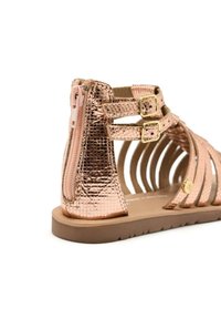 Sandalias metálicas en color oro rosa que cuentan con dos correas ajustables con hebillas, un cierre trasero con cremallera y una suela de goma plana con detalles en el lado recortados.