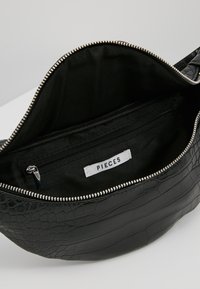 Svart faux läder crossbody-väska med krokodilmönster, dragkedjestängning och svart foder som har ett innerfack och etikett.