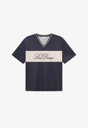 Mornarica mrežasta majica s kratkim rukavima i V-izrezom, s krem horizontalnom trakom na sredini na kojoj je crnim slovima napisano "Les Deux". Labav kroj.