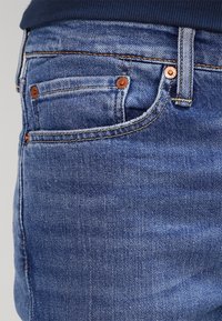 Blå denimjeans med en klassisk femfickdesign, kopparfärgade nitar och en mjuk textur med subtila blekningar.