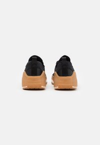 Černé tenisky s světlým hnědým gumovým podešvím, vršek z texturované tkaniny a poutka na zadní straně pro snadné obouvání.