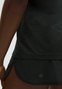 Top atlético negro con rayas texturizadas, combinado con pantalones cortos negros con aberturas y un logotipo tonal. Enfoque en materiales ligeros y transpirables.