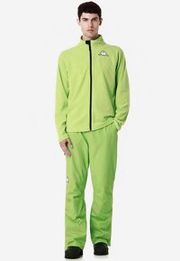Giacca con zip in pile verde con pantaloni abbinati, presenta un logo sul petto e un piccolo logo sulla gamba del pantalone. Zip e polsini neri.