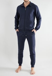 Navy blue tracksuit made of soft cotton, featuring a zip-up jacket with a collar and pants with an elastic waistband and cuffed ankles.