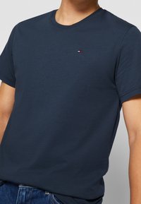 Navy blue cotton t-shirt with a round neckline, short sleeves, and a small logo featuring red, white, and blue stripes on the chest.