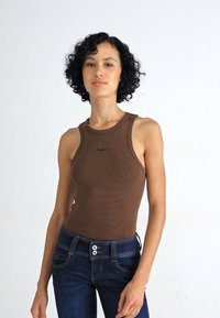 Bruine aansluitende tanktop met een ronde halslijn en smalle bandjes, gecombineerd met donkerblauwe jeans met een knoopsluiting en voorkruiszakken.