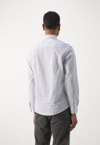 Camicia bianca con motivo a pois blu, maniche lunghe e colletto dritto, abbinata a pantaloni in velluto a coste grigio scuro.