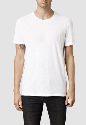 Maglietta bianca a maniche corte, con collo rotondo, realizzata in tessuto leggero, caratterizzata da una texture morbida e una vestibilità rilassata. Indossata con jeans neri.