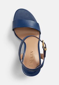 Blå läder sandal med ett brett tåband och ett smalt ankelband. Har en spänne i guldton och en slät, neutral innersula.