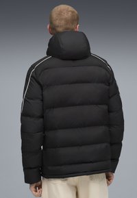 Sort pufferjakke med høj krave, kviltet design og hvide accentstriber langs skuldrene. Blød, glat tekstur.