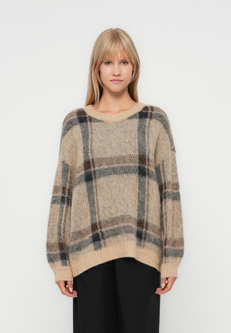 Beige wollen sweater met een geruit patroon met bruine en donkergrijze accenten. Losse pasvorm, brede mouwen en geribbelde manchetten.