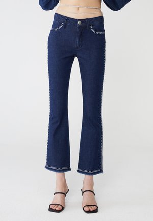 Jeans svasati in denim scuro con cuciture a contrasto bianche, design a cinque tasche e orlo leggermente sfilacciato per un effetto testurizzato.