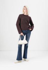 Maglione lavorato a maglia color bordeaux, jeans blu svasati, borsa a tracolla bianca e sneakers bianche. Il maglione presenta un collo rotondo e maniche lunghe.