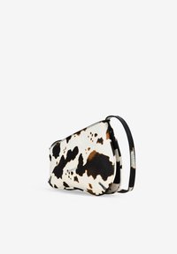 Bolso cruzado de piel de vaca con una base blanca y manchas negras y marrones, un diseño elegante y una delgada correa negra.