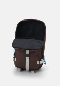 Brauner Nylon-Rucksack mit schwarzem Innenraum, einem Reißverschluss-Frontfach und hellblauen Akzenten. Verfügt über verstellbare Träger und seitliche Hardware-Befestigungen.