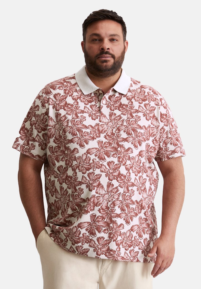 Polo à manches courtes en tissu léger avec un fond rose et un motif floral rouge. Comprend un col blanc et une coupe décontractée.