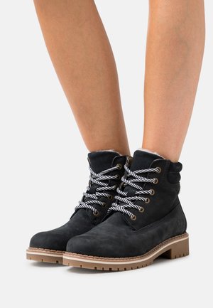 Black suede ankle boots with a textured finish, featuring contrasting gray and white laces, padded collar, and a sturdy tan rubber sole.