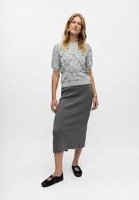 Pull en maille grise avec des manches bouffantes courtes, associé à une jupe midi grise cintrée ; le mannequin porte des chaussures noires avec des découpes.
