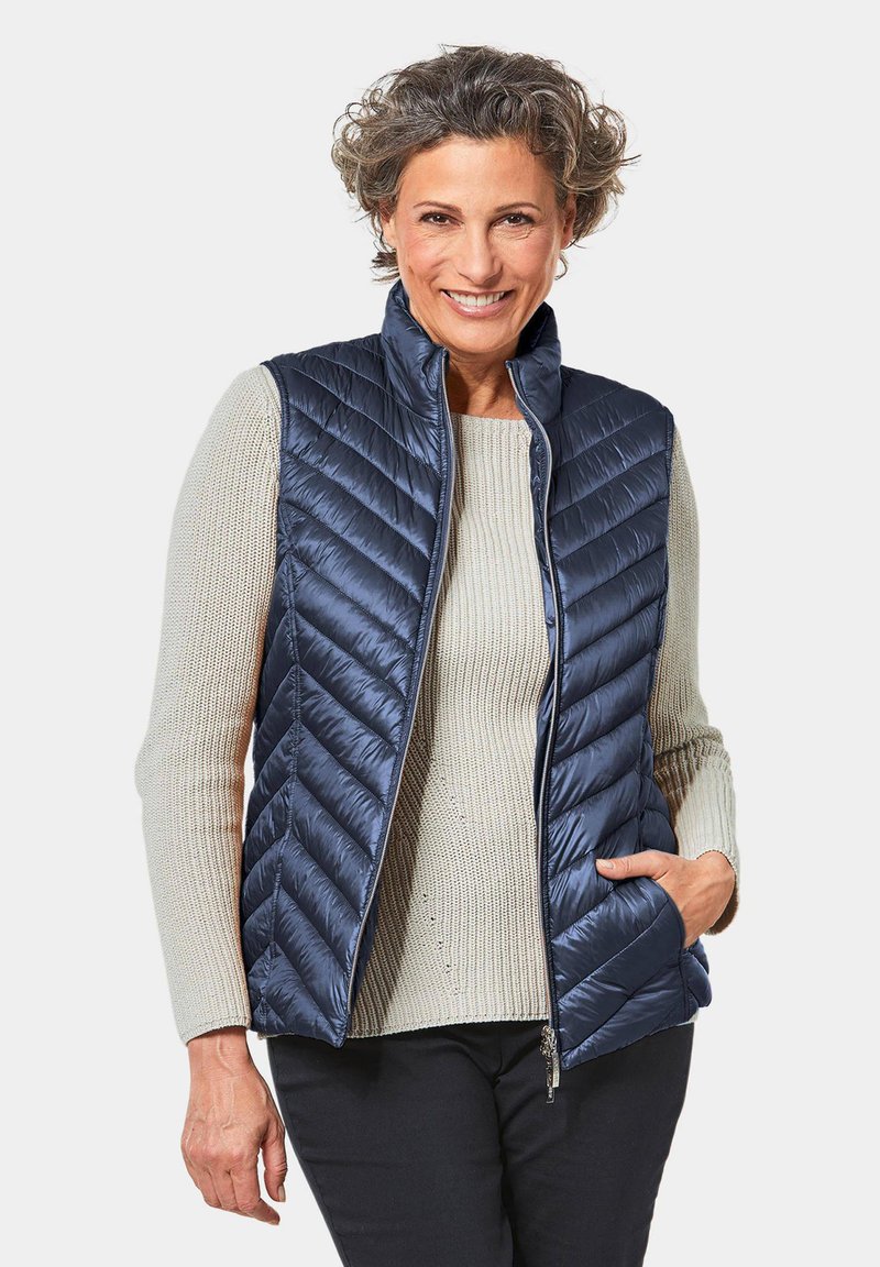 Navy-gestepptes Weste mit Reißverschluss und hohem Kragen, getragen über einem hellbeigen Strickpullover. Verfügt über Seitentaschen und ein schlankes Design.