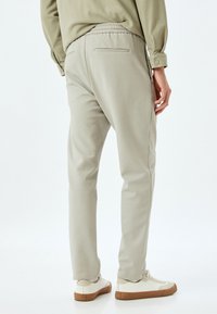 Lysbeige sweatpants med elastisk talje, smalle ben og en baglomme, som er parret med hvide sneakers med brune såler.