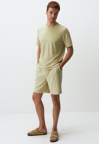 Jasnozielona koszulka z krótkim rękawem i dopasowane szorty z miękkiej, teksturowanej tkaniny. Beżowe klapki dopełniają strój.