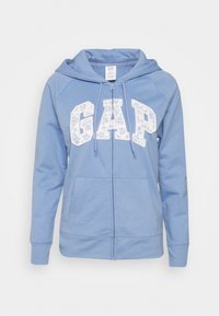 Haut de hoodie zippé bleu clair avec logo "GAP" à motifs floraux, poches avant et capuche avec cordon de serrage. Matériau en coton doux avec poignets côtelés.