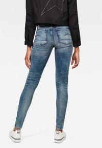 Tunnhäftiga blå denimjeans med en blekt tvätt, bakfickor med sömnadsdetaljer och synliga veck. Kombinerat med vita sneakers.