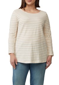 Gestreepte lange mouwen shirt in crème en beige tinten, ronde halslijn, zachte textuur, met een losse pasvorm en kromme zoom. Gecombineerd met blauwe jeans.