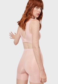 Helles rosa BH- und Shorts-Set aus glattem, dehnbarem Stoff. Der BH hat einen tiefen Rücken und verstellbare Träger; die nahtlosen Shorts reichen bis zur Mitte des Oberschenkels.