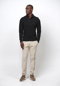 Schwarzes langärmliges Poloshirt, beigefarbene Chinos und braune Turnschuhe. Schlichtes Design mit schlanker Passform und gerippten Bündchen. Einheitliche Textur, keine sichtbaren Muster.