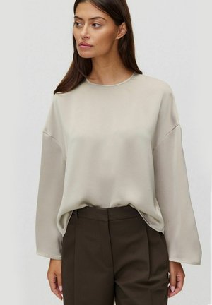 Licht beige lange mouw top met een ronde hals, gemaakt van gladde stof; gecombineerd met bruin op maat gemaakte broek, met een ontspannen pasvorm en verlaagde schouders.