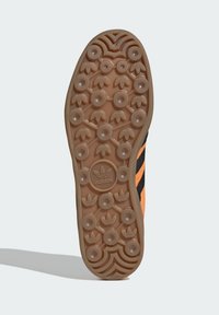 Crna i narančasta guma pričvršćena na dnu patika s kružnim uzorcima za st grip, od gumenog materijala, s centralnim adidas logotipom. Ravna, teksturirana i izdržljiva konstrukcija.