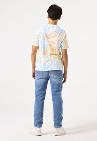 Camisa de manga corta con patrón abstracto multicolor en tonos pastel; combinada con jeans azul claro y zapatillas blancas.