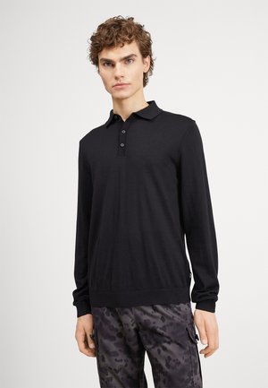 Cămașă polo neagră cu mâneci lungi, având un guler clasic, placket cu trei butoane, manșete ribbate și o textură netedă de tricot. Asortată cu pantaloni cu model.