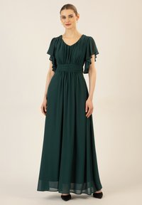 Maxikleid in tiefgrün, aus leichtem Stoff gefertigt. Verfügt über plissierte kurze Ärmel, eine figurbetonte Taille und einen fließenden Rock mit einem subtilen Glanz.