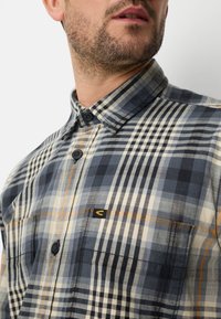 Geruit overhemd in blauw-, wit- en oranje tinten; gemaakt van zachte stof; voorzien van een geknoopte kraag, borstzak en logopatch.