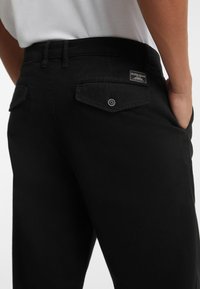 Schwarze Jeans aus Denim mit einer figurschmeichelnden Passform, aufgesetzten Taschen mit Knopfverschlüssen und einem Markenlabel über der rechten Tasche.